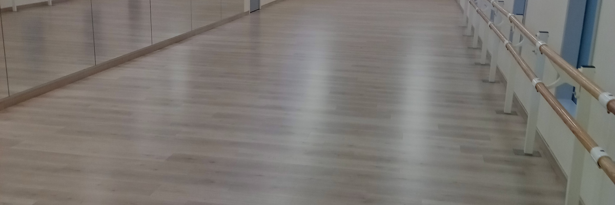 Salle spacieuse avec plancher en bois, miroirs et barres.