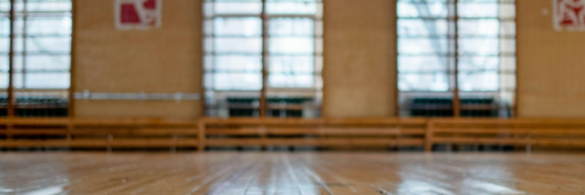 Salle de sport avec parquet, fenêtres et panneaux.