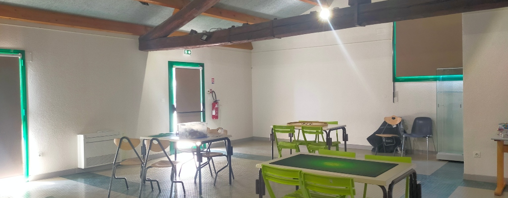 Salle avec tables, chaises, radiateur, extincteur, porte-manteau et armoire.