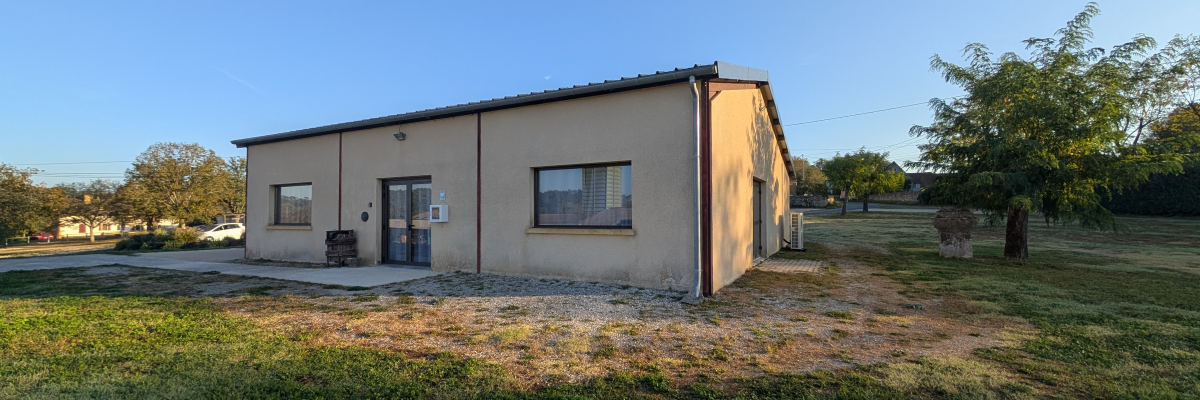 Bâtiment bas avec porte et fenêtres, situé dans une zone herbeuse.