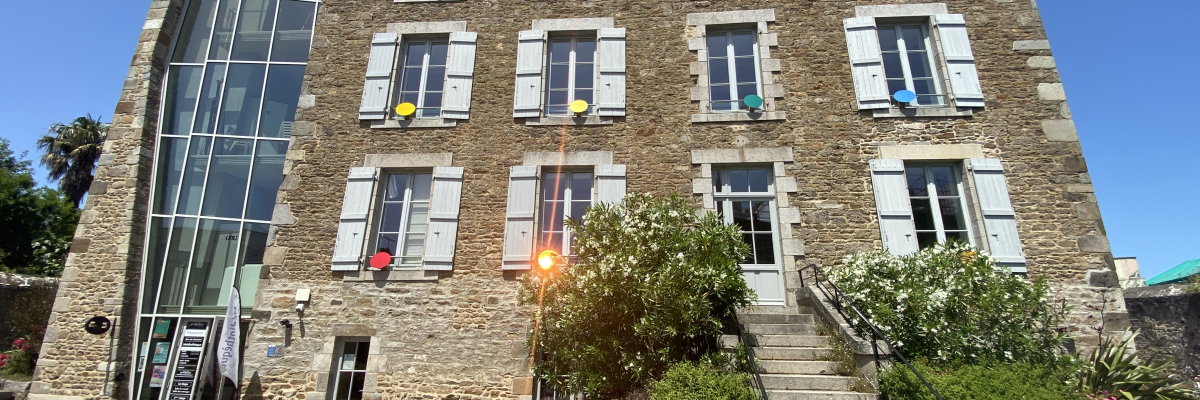 Bâtiment en pierre avec plusieurs fenêtres, portes vitrées, escaliers et fleurs.