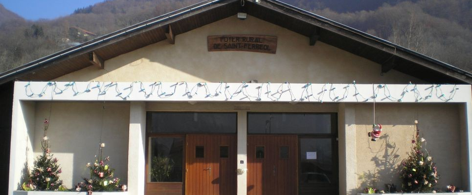 Bâtiment avec porte en bois double, porte plus petite, décorations florales, enseigne, montagnes en arrière-plan.