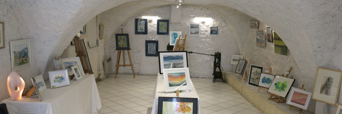 Galerie d'art avec peintures, chevalets, tables et chaises.