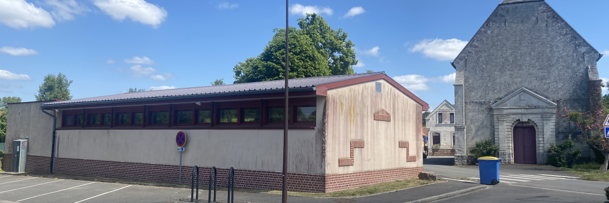 Bâtiment avec structure en bois, parking, poubelle, lampadaire, église en pierre.