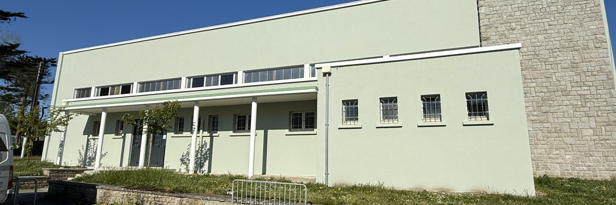 Bâtiment avec façade beige, fenêtres et porte avec rampes d'accès.