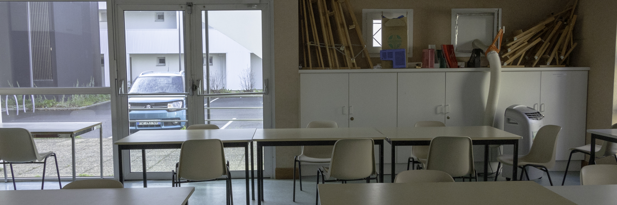 Salle avec tables, chaises, meubles de rangement, escabeau, fenêtre et porte vitrée.