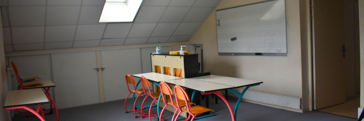 Salle de classe avec table, chaises, tableau blanc et armoire.