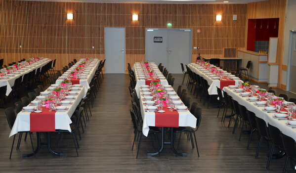 Salle de banquet avec tables, chaises, nappes, vaisselle et fleurs.