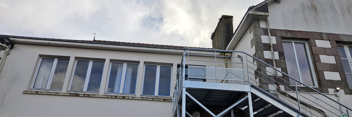 Bâtiment avec escaliers extérieurs et voitures garées.