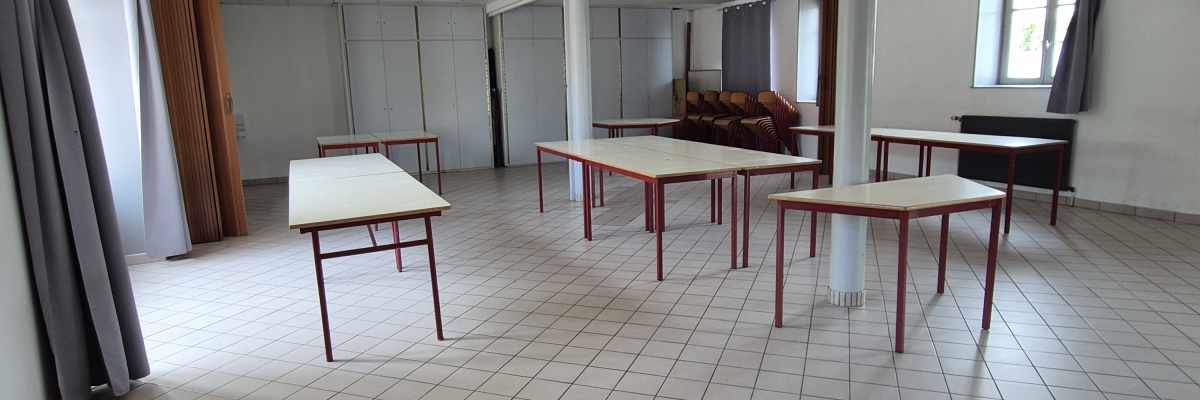 Salle vide avec tables, chaises, plantes et lumières au plafond.