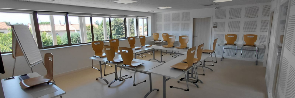 Salle avec tables, chaises, tableau blanc et ordinateur.