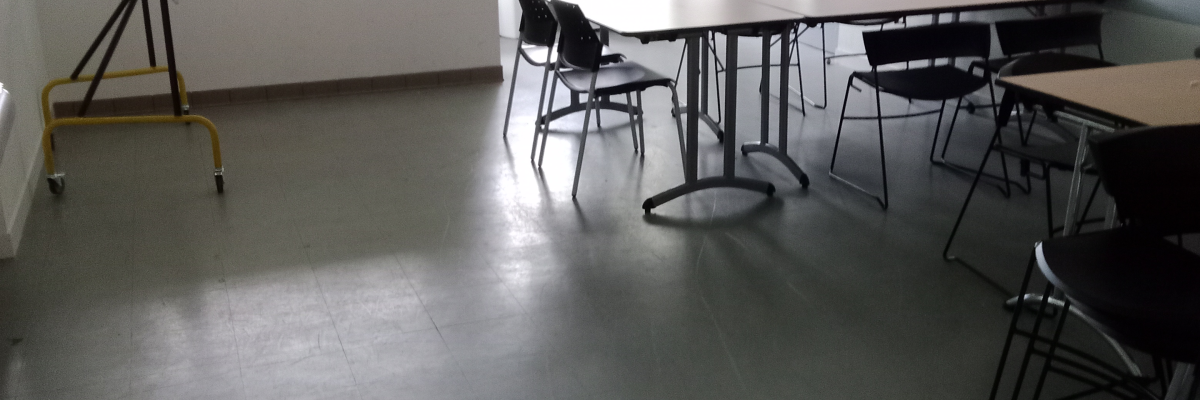 Salle avec tables, chaises, chevalet et fenêtres.