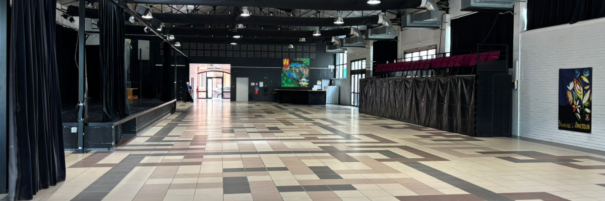 Salle spacieuse avec sol carrelé, éclairage suspendu, rideaux noirs et affiches murales.