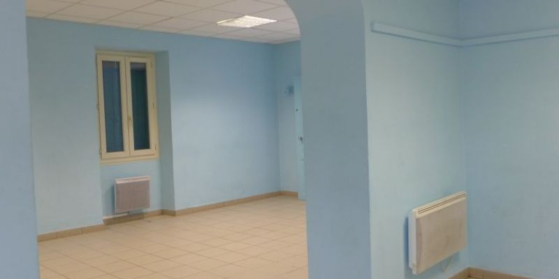 Pièce vide, murs bleus, carrelage beige, radiateurs, fenêtre et plafond avec lumières.