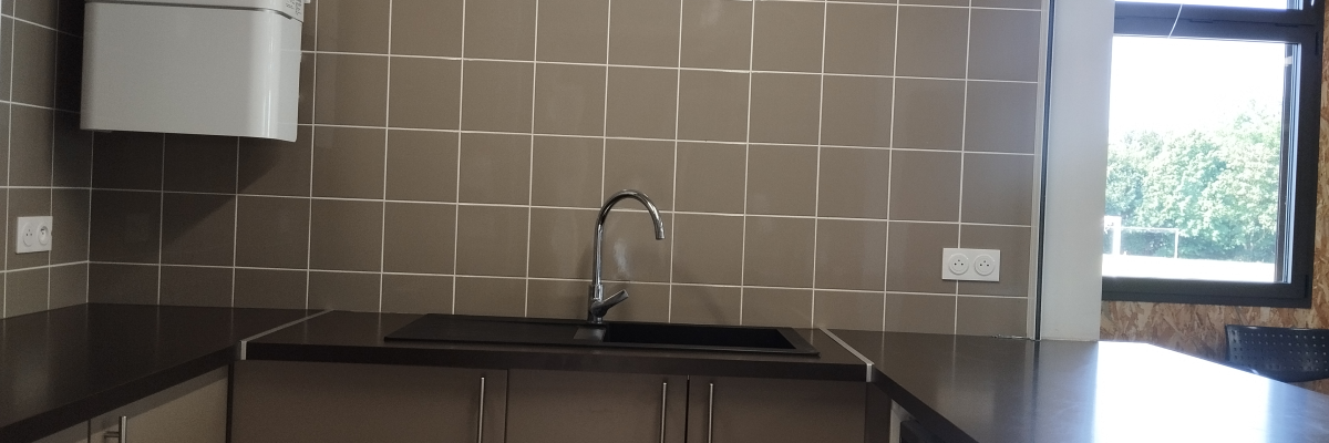 Cuisine avec évier, plan de travail, armoires, chauffe-eau et réfrigérateur.