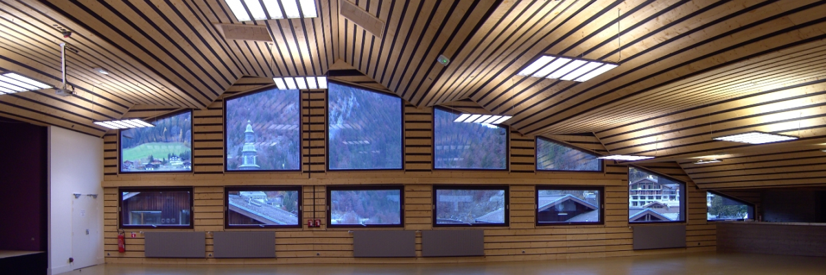 Salle spacieuse avec grandes fenêtres, projecteurs et bancs.