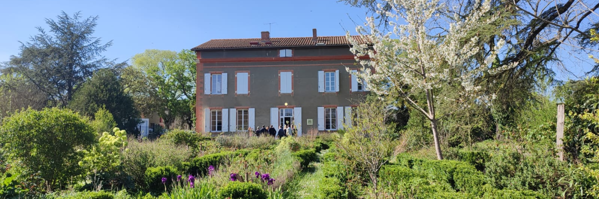 Maison à deux étages avec jardin, arbres et buissons.