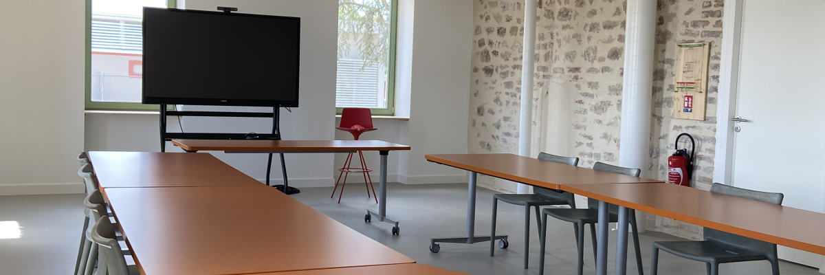 Salle avec tables, chaises, écran, et projecteur.