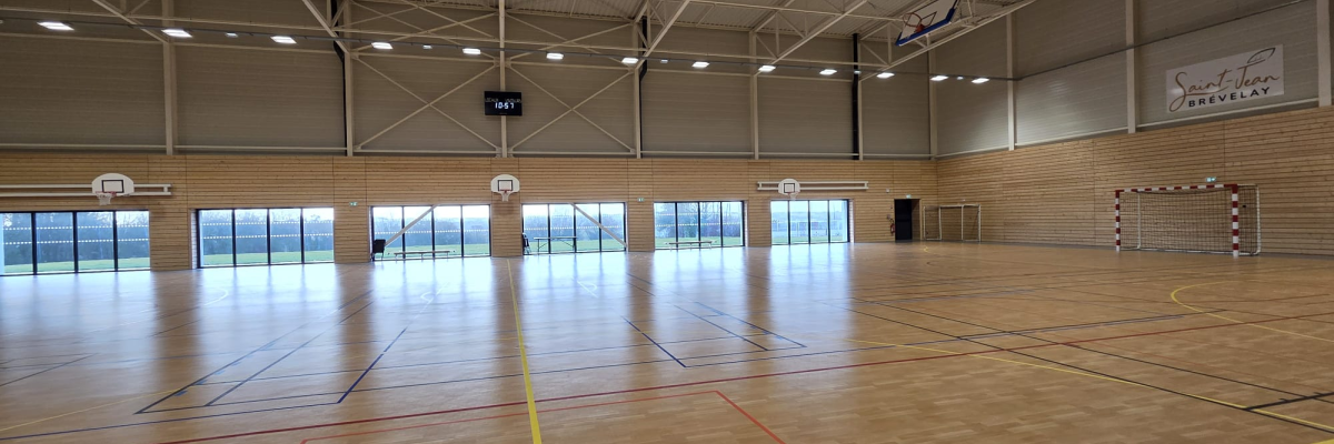 Salle de sport avec parquet, lignes de jeu, paniers de basket, murs et fenêtres.