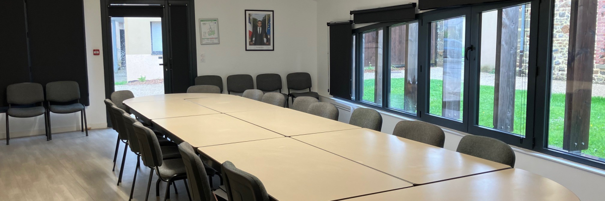 Salle de réunion avec table, chaises, vidéoprojecteur et grandes fenêtres.