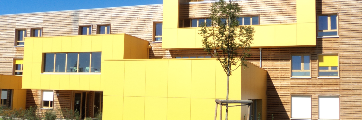 Immeuble jaune avec arbre, parking et vélo.