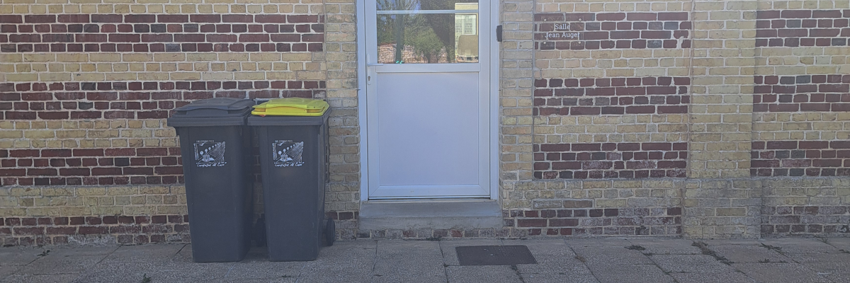 Mur de briques avec porte blanche, poubelles, allée en béton.
