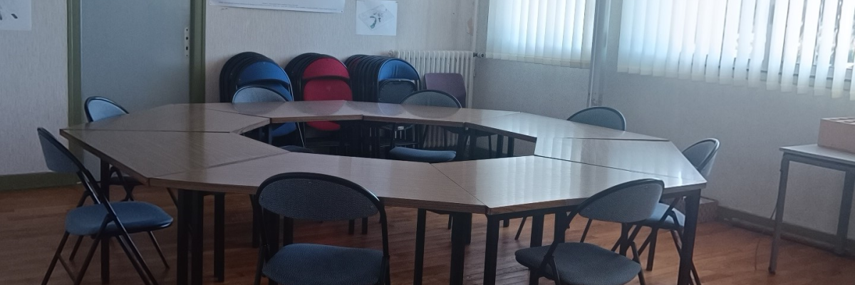 Salle avec table, chaises, tableau blanc, radiateurs et fenêtres.