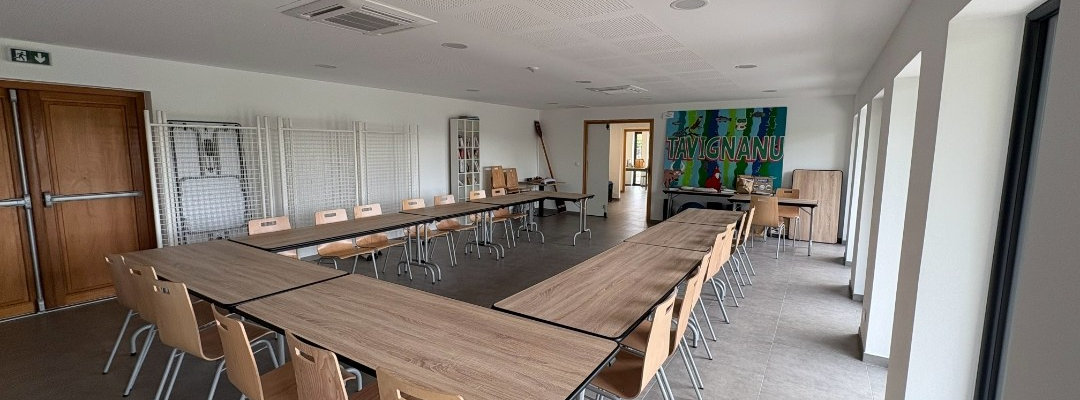 Salle avec tables en L, chaises, tableau et portes.