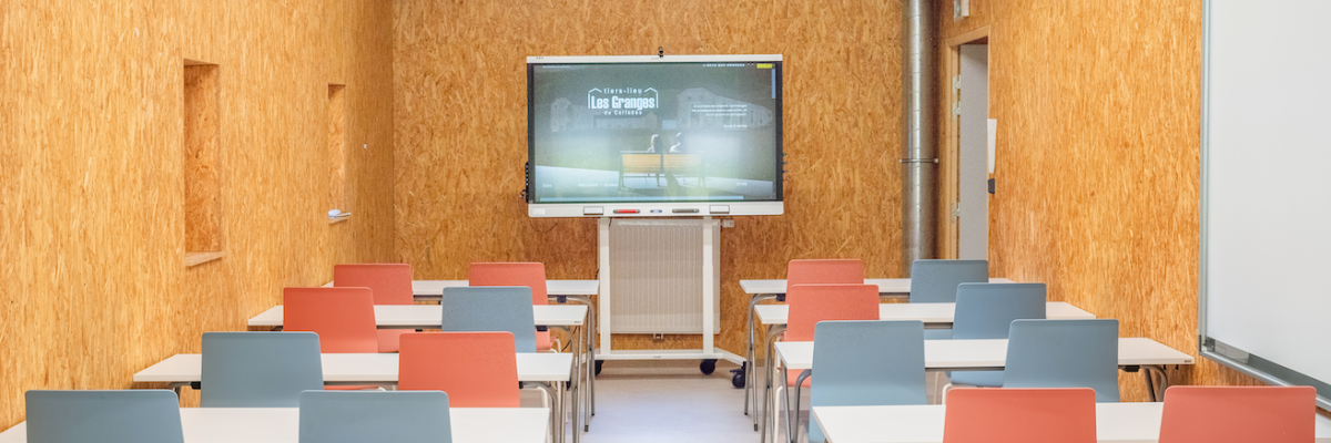 Salle de classe avec tables, chaises, tableau blanc, écran et vidéoprojecteur.