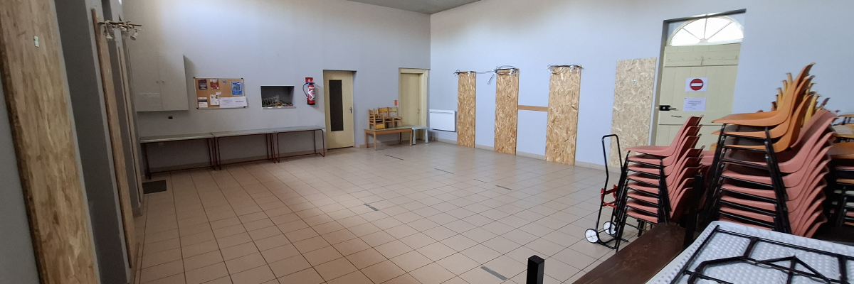 Salle avec tables, chaises empilées, chariot, et matériel de rangement.