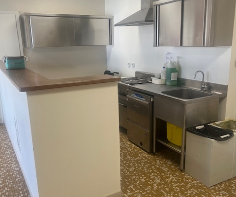 Cuisine avec plan de travail, quatre brûleurs, hotte, évier, frigo et meuble de rangement.