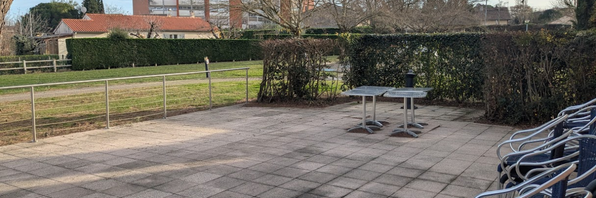 "Espace extérieur avec tables, chaises, terrain gazonné et bâtiment en arrière-plan."