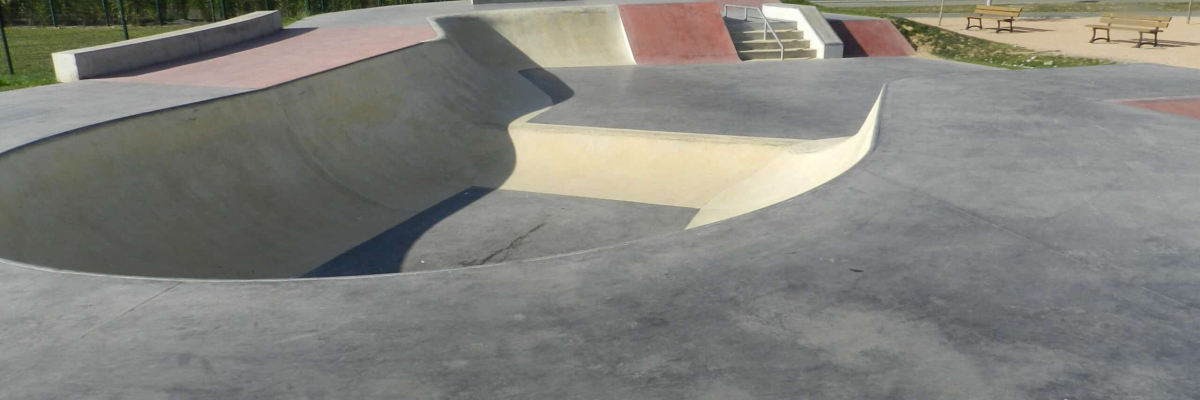 Skatepark avec rampes, bowl et bâtiment en arrière-plan.