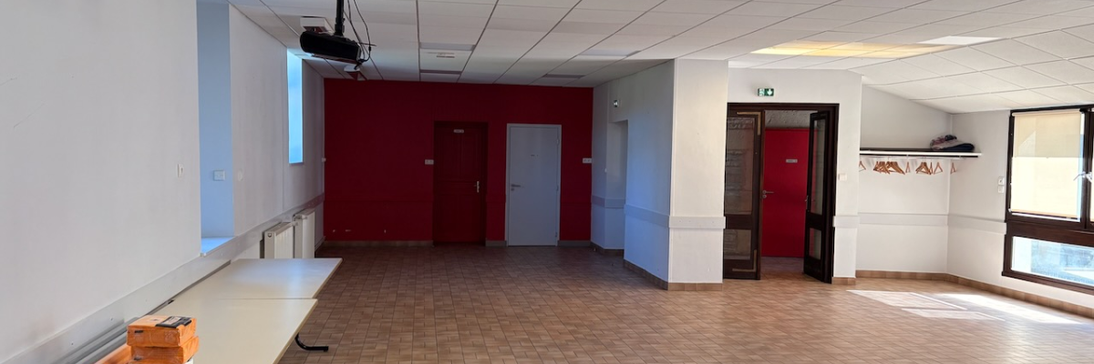 Salle avec tables, chaises, projecteur, portes et fenêtres.