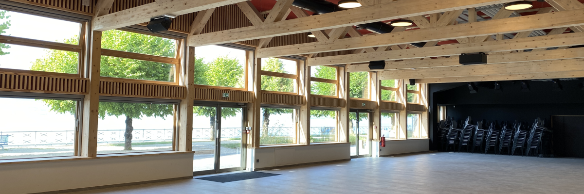 Salle spacieuse avec chaises, grandes fenêtres et structure en bois.