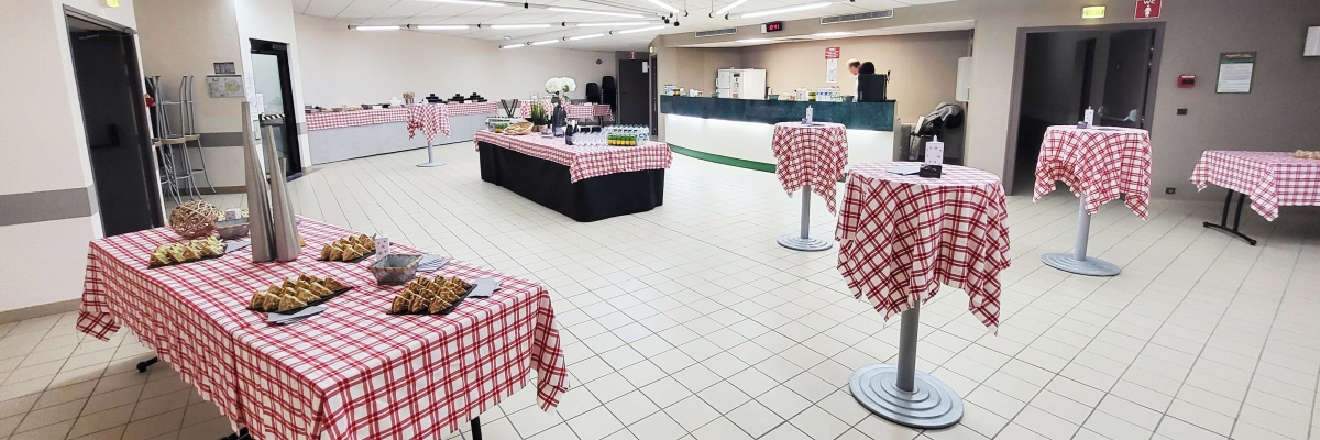 Salle avec tables à nappes à carreaux, nourriture, tables hautes, porte-manteaux.