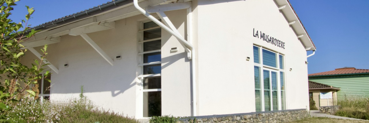Bâtiment blanc avec toit rouge, grandes fenêtres, murs en pierre, jardin sec.