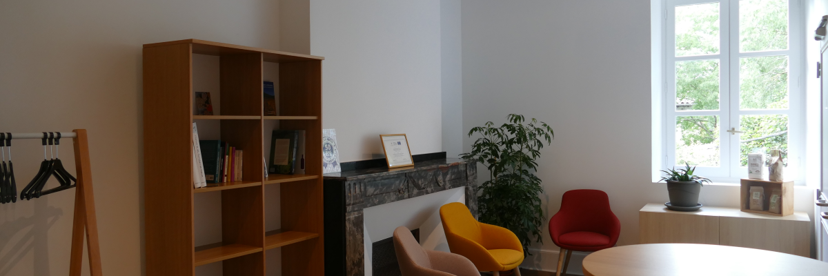 Pièce avec étagères, chaises, table ronde, plantes, cheminée et porte-manteau.