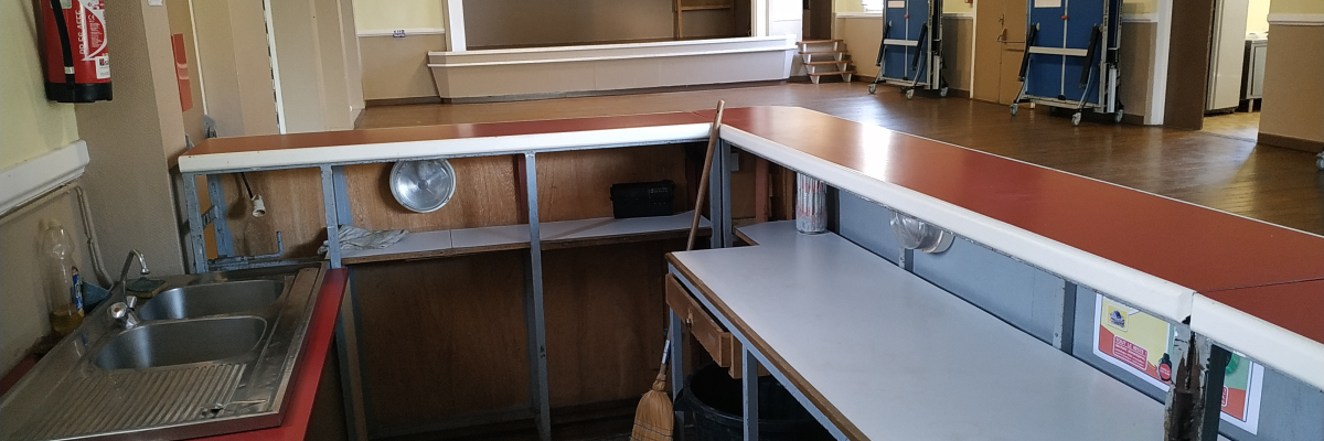 Salle avec évier, tables, chaises, chariots et extincteur.