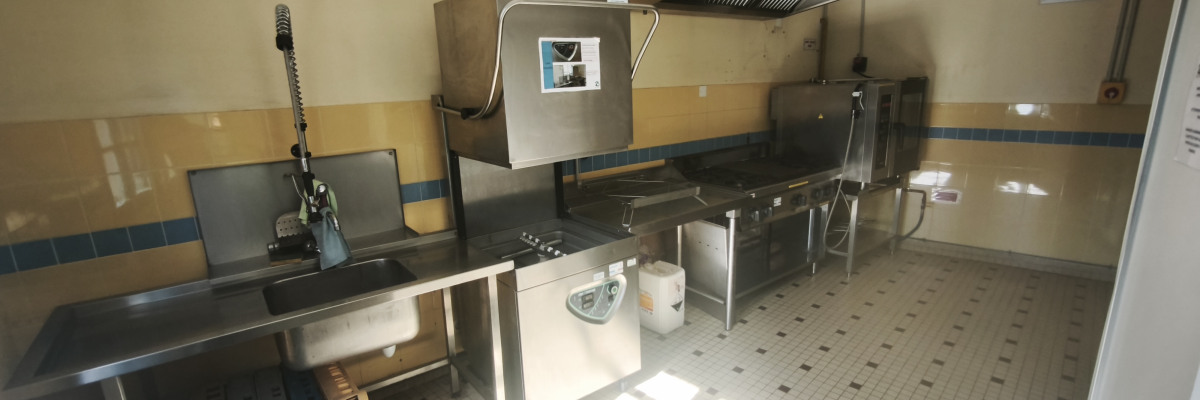 Cuisine équipée avec plans de travail, évier, lave-vaisselle, four, hotte, réfrigérateur et étagères.