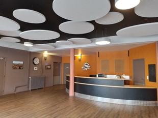 Salle avec luminaires ronds, comptoir courbe, miroir, radiateur, porte et horloge murale.
