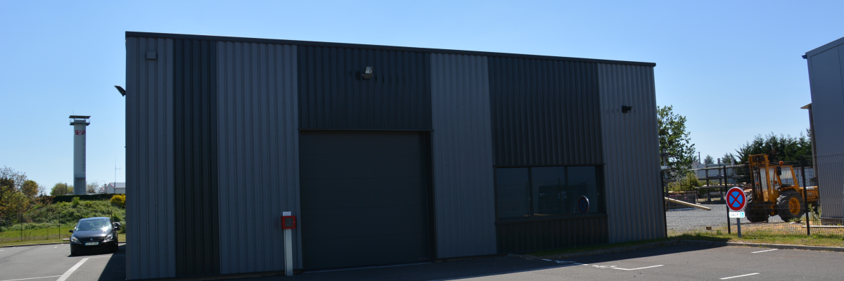 Bâtiment industriel avec porte de garage, voiture, panneau de stationnement et engin de chantier.