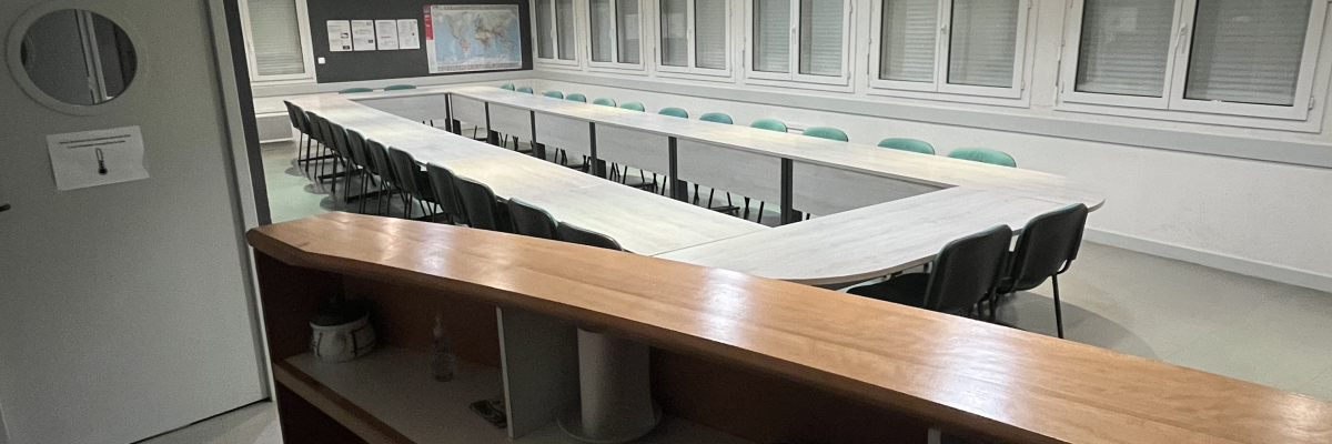 Salle de réunion avec table, chaises, tableau blanc et fenêtres.