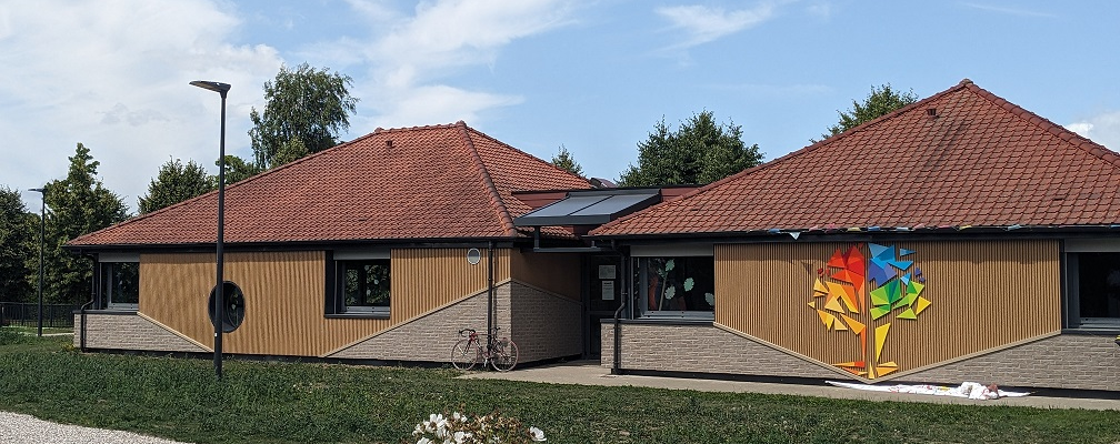 Bâtiment avec toits rouges, murs en bois, panneaux solaires, graffiti, vélo, réverbère, fleurs.