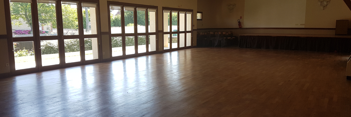 Salle vide avec parquet, fenêtres et murs blancs.