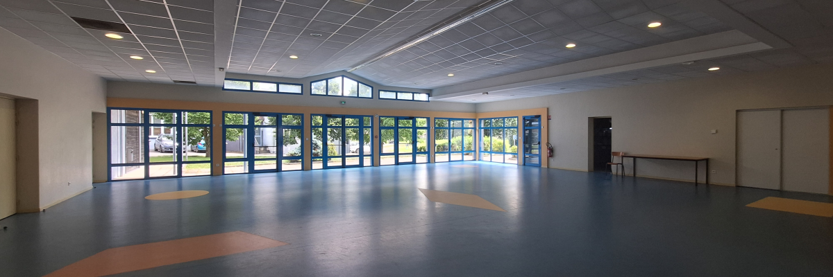 Salle vide avec grandes fenêtres, portes et taches au sol.