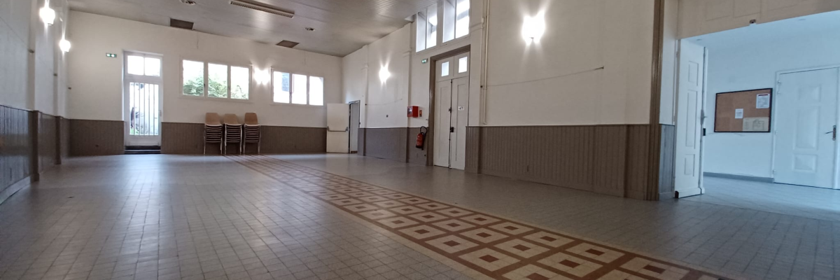 Salle vide avec sol carrelé, murs en bois et blanc, portes et fenêtres. Éclairage suspendu au plafond.