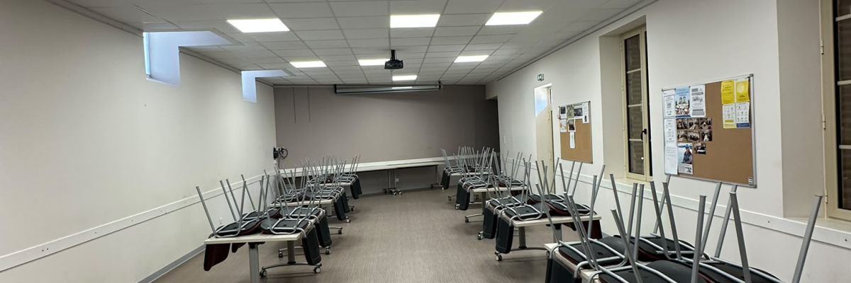 Salle de classe avec tables, chaises, tableau blanc et projecteur.
