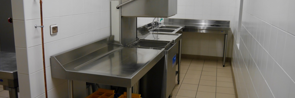 Cuisine professionnelle avec plans de travail en inox, éviers, hottes, et étagères avec bacs en plastique.