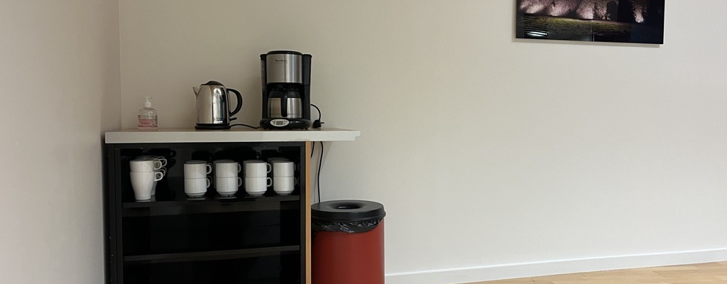 Coin cuisine avec machine à café, bouilloire, tasses, et poubelle.